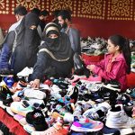 Women purchasing jogger shoes from a vendor at Makki Shah Road.
