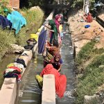 Women wash clothes using running tube-well water near Hala Naka Road.