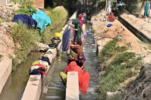 Women wash clothes using running tube-well water near Hala Naka Road.