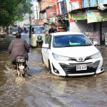 Commuters passing through rain water accumulated on the station road after heavy rain in the city.
