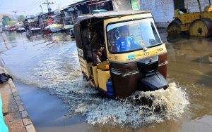 Commuters passing through rain water accumulated on the station road after heavy rain in the city.