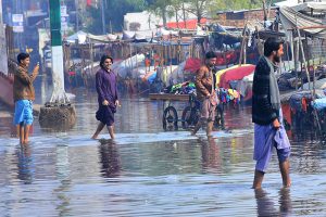 Commuters passing through rain water accumulated on the station road after heavy rain in the city.
