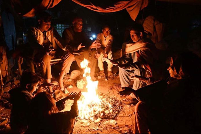 Citizens warm themselves around a fire to beat the cold at Jinnah Colony