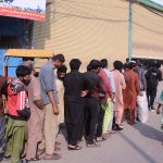 People stand in a queue waiting to receive free food distributed by volunteers