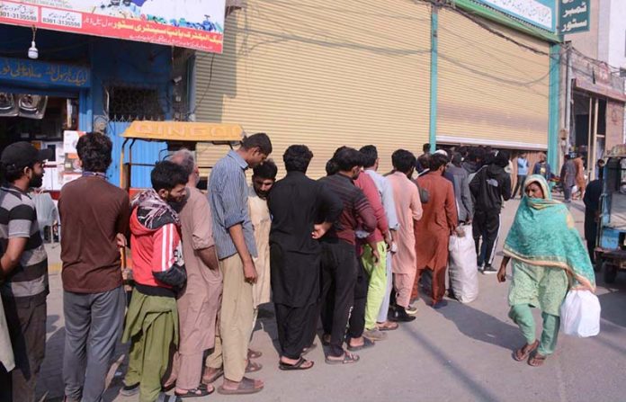 People stand in a queue waiting to receive free food distributed by volunteers