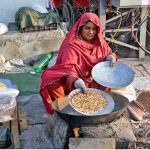 A woman street vendor roasting peanuts and corn kernels, attracting passersby with the aroma of freshly roasted snacks for selling in the roadside her setup.