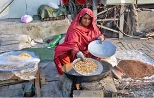 A woman street vendor roasting peanuts and corn kernels, attracting passersby with the aroma of freshly roasted snacks for selling in the roadside her setup.