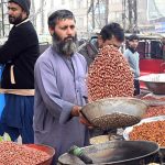 A vendor roasts peanuts at his roadside stall to attract customers.