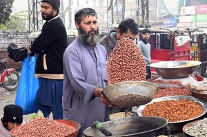 A vendor roasts peanuts at his roadside stall to attract customers.