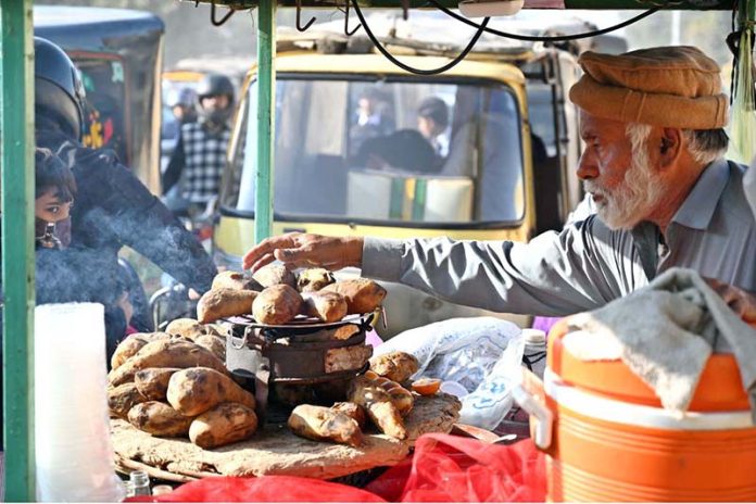 A vendor sells hot roasted yums drizzled with spicy sauce from his cart near Rahmatul-il-Alamin Park, Satellite Town