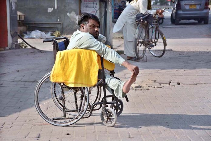 A differently-abled vendor waits in his wheelchair for customers along the roadside, displaying dusters on his cart for sale on the occasion of the International Day of Persons with Disabilities