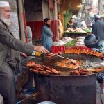 An elderly vendor roasts and displays fish to attract customers during the winter season at Ghanta Ghar.