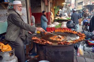 An elderly vendor roasts and displays fish to attract customers during the winter season at Ghanta Ghar.