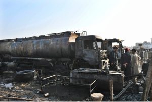 People stand in front of oil tankers burned at the Keamari Oil Terminal