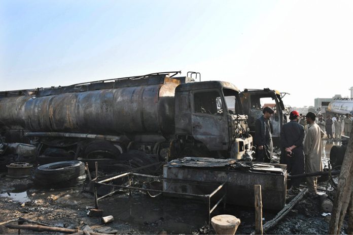 People stand in front of oil tankers burned at the Keamari Oil Terminal