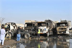 People stand in front of oil tankers burned at the Keamari Oil Terminal