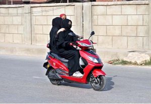 Two veiled girls ride a scooter through the city without wearing helmets, violating traffic safety rules.