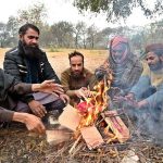 People are sitting around fire to keep themselves warm during cold weather in the Federal Capital