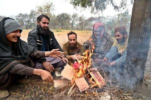 People are sitting around fire to keep themselves warm during cold weather in the Federal Capital