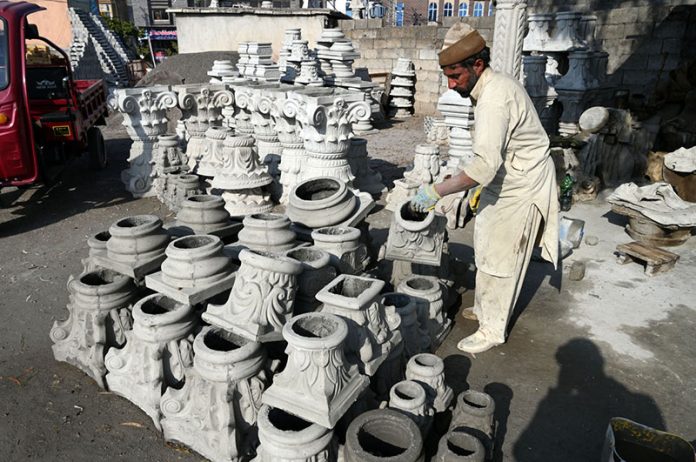 A craftsman arranges freshly molded concrete pillar capitals at a roadside workshop, where decorative architectural elements are being prepared for construction use