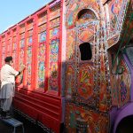 A painter applies intricate traditional designs while painting the body of a delivery truck at his workplace near Pirwadai