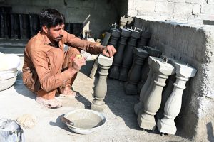 A craftsman arranges freshly molded concrete pillar capitals at a roadside workshop, where decorative architectural elements are being prepared for construction use