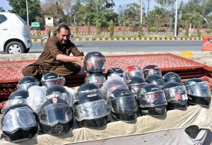 A roadside vendor waits for customers while displaying helmets, an essential safety requirement for riders of motorbike, on a busy city road.