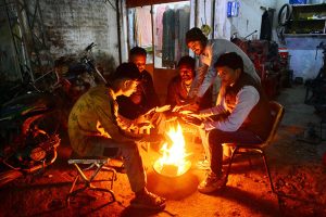 People gather around a roadside fire to keep warm amid chilly weather in the city.