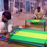 Craftsmen weaves a traditional charpai using colorful threads, preserving a centuries-old handicraft