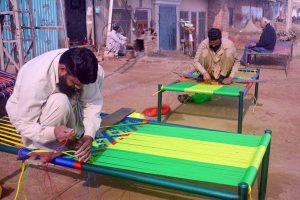 Craftsmen weaves a traditional charpai using colorful threads, preserving a centuries-old handicraft