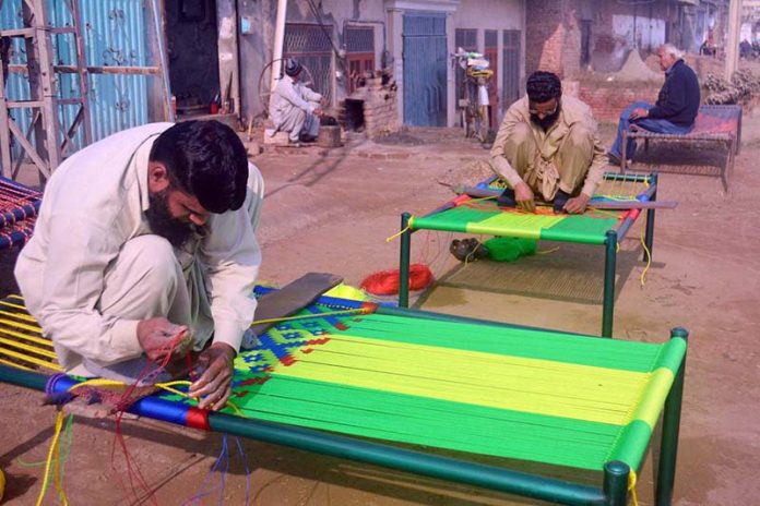 Craftsmen weaves a traditional charpai using colorful threads, preserving a centuries-old handicraft