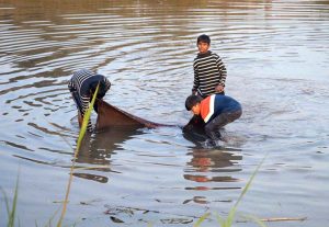 Children trying to catch fish with piece of cloth in a canal.