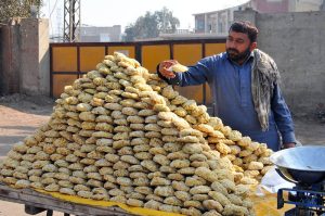 A street vendor neatly arranges blocks of traditional sweet gur (jaggery) on his wooden cart for sale at a local market.
