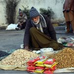 An elderly vendor sells peanuts and dry fruits on the roadside to attract passersby and earn a living in the local market