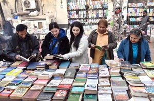 People selecting and purchasing old books from a stall along Mall Road in Provincial Capital.