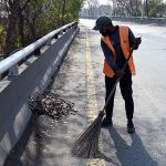 A CDA sanitary worker cleans dry leaves fallen from trees along a roadside after winter rain as the sun shines in the federal capital