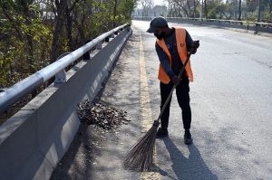 A CDA sanitary worker cleans dry leaves fallen from trees along a roadside after winter rain as the sun shines in the federal capital