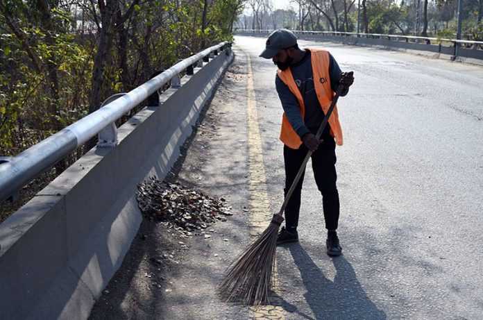 A CDA sanitary worker cleans dry leaves fallen from trees along a roadside after winter rain as the sun shines in the federal capital