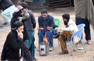 People are sitting around fire to keep themselves warm during cold weather in the Federal Capital