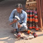 An artisan carefully carves part of traditional wooden bed craft by hand at his roadside workshop in the city