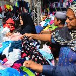 Women selecting and purchasing old warm clothes from vendor during winter season.