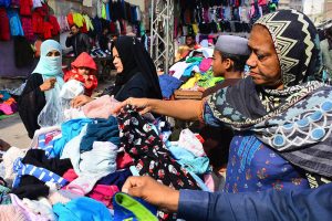Women selecting and purchasing old warm clothes from vendor during winter season.