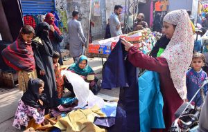 Women selecting and purchasing old warm clothes from vendor during winter season.