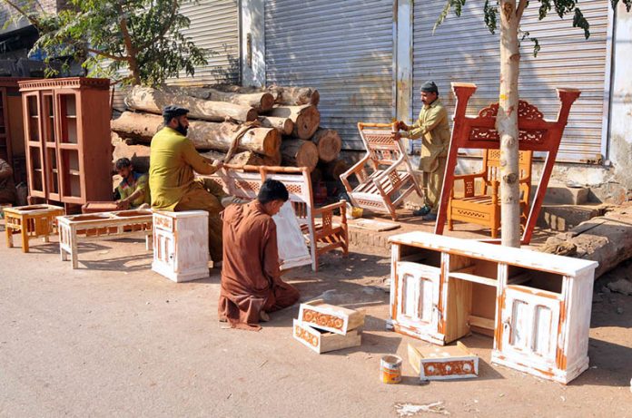 Carpenters apply primer to furniture before polishing at his workplace in the city