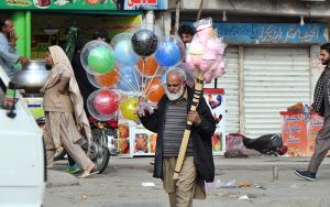 An elderly vendor displaying balloons and cotton candy to attract the customers in a local market.