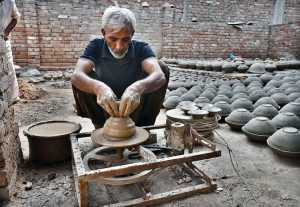 A woman paints a clay-made pitcher after preparing it at her workplace in Kumharpara.