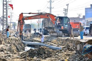 Labourers busy in construction work of sewerage pipe line with help of heavy machine at autobahn road during development work in the city.