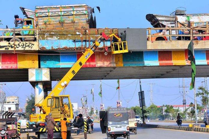 HMC workers are busy installing an LED screen for advertisements on the bypass bridge, using heavy machinery on Jamshoro Road