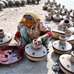 A woman paints a clay-made pitcher after preparing it at her workplace in Kumharpara.