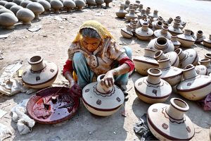 A woman paints a clay-made pitcher after preparing it at her workplace in Kumharpara.